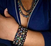 Close up of person with shirt unzipped, revealing iridescent beaded necklaces and bracelets.
