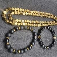 Shiny gold long beaded jewelry laying on the same table as two black and gold beaded bracelets. 
 