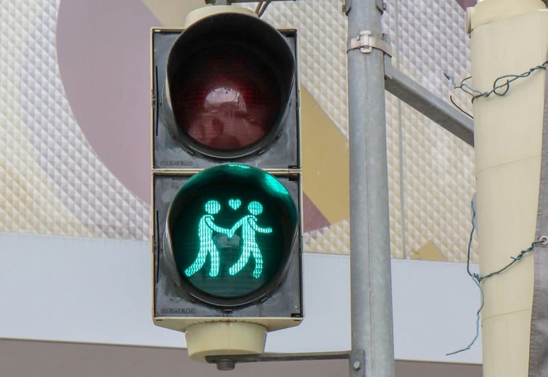 A traffic light has a green bulb with a shape overlayed that looks like two people holding hands with a heart between them.