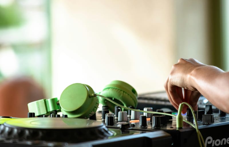 A brown skinned person on the DJ turn tables with green headphones