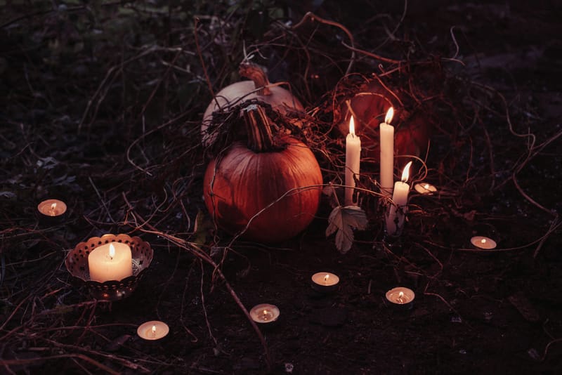 Two pumpkins at night time in the woods, surrounded by candles. 